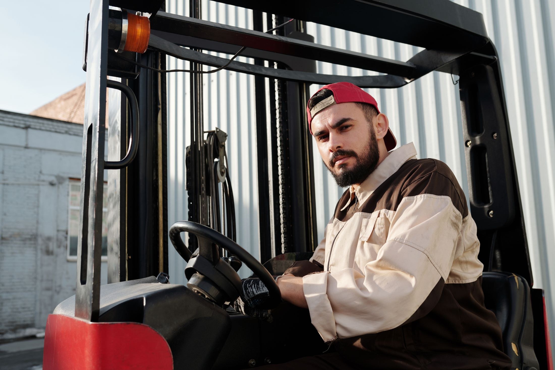Operator wearing gloves sits at forklift controls outside an industrial building