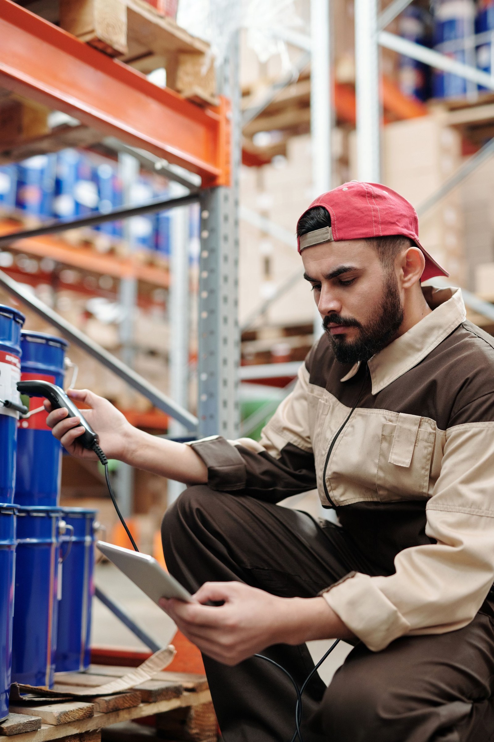 Warehouse worker checks goods with a handheld barcode scanner and tablet beside stocked pallet racks